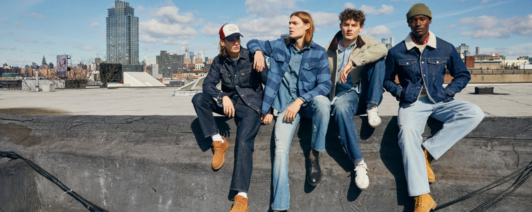 Four men sitting on a concrete fence wearing jeans