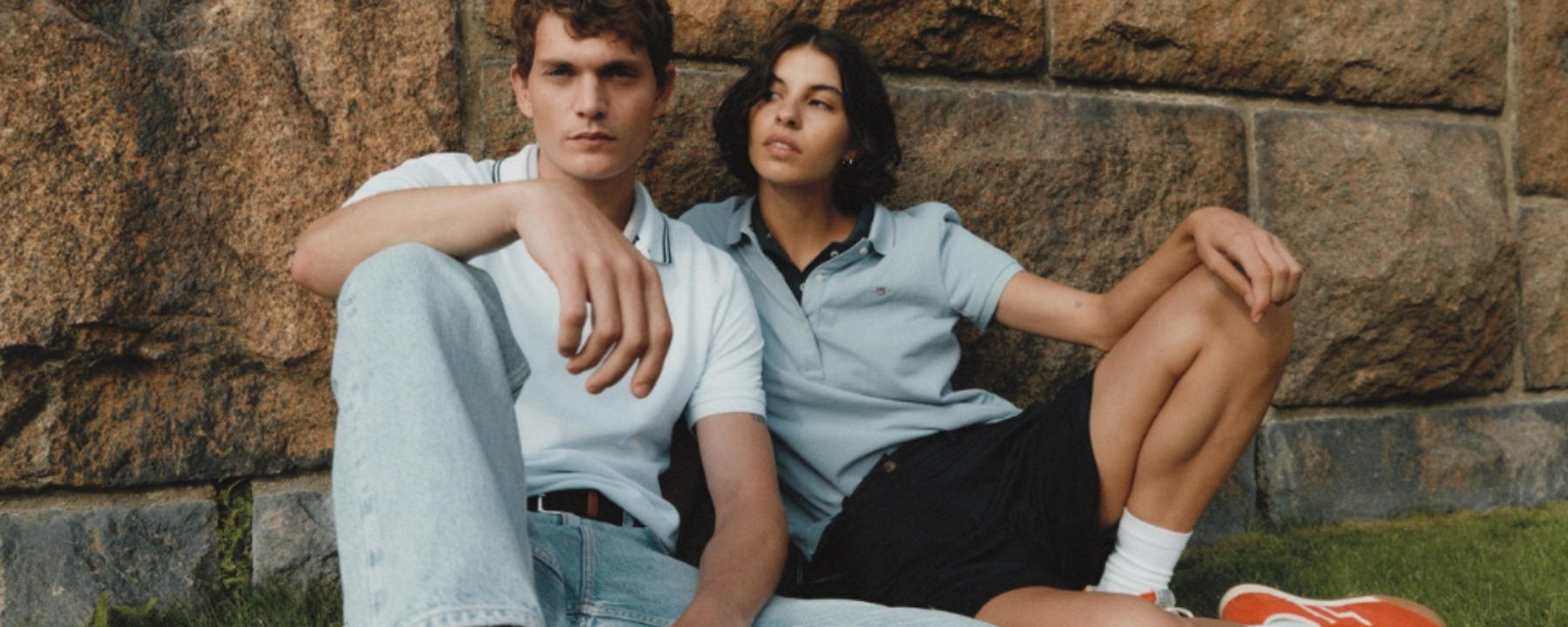 man and woman leaning against a brick wall