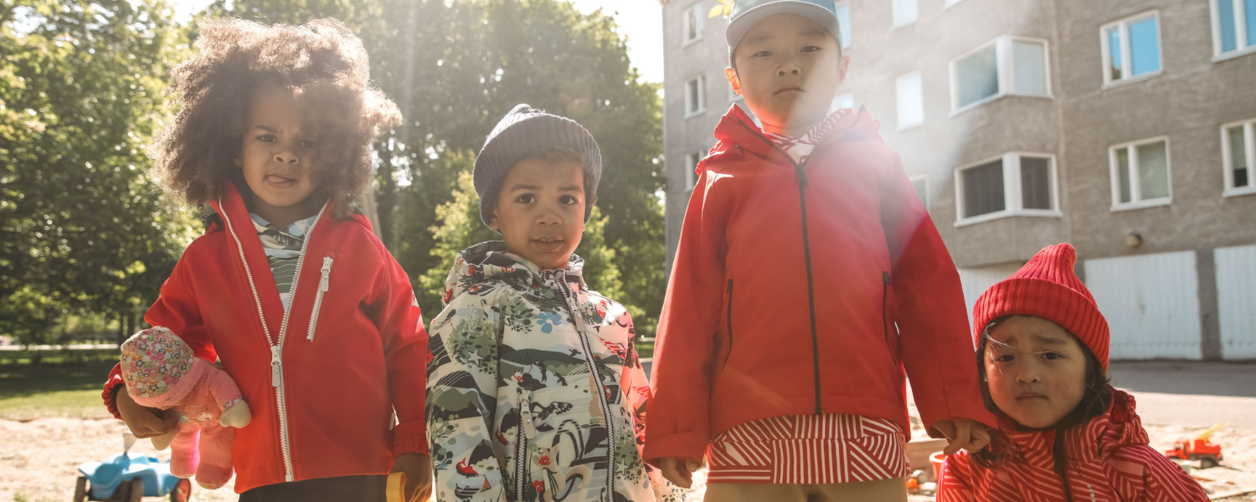 Neljä lasta seisoo takit päällä hiekkalaatikolla