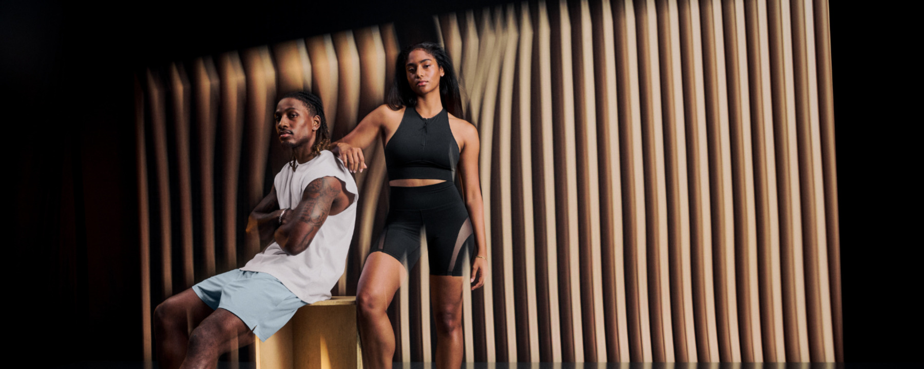Women and man in athletic clothes by a wooden panel wall.