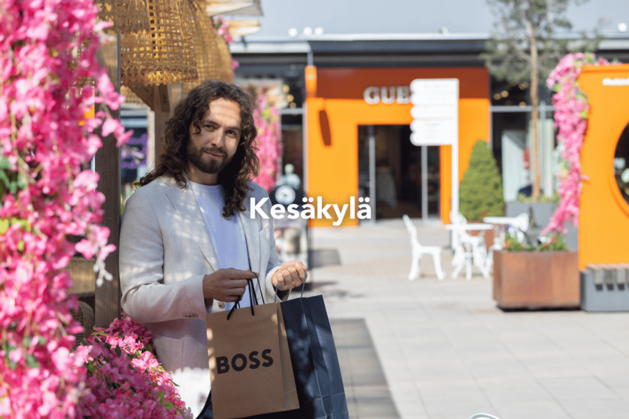 Mies kädessään ostoskasseja Helsinki Outletin Keskusaukiolla, joka on koristeltu kesäisen kukkaiseksi