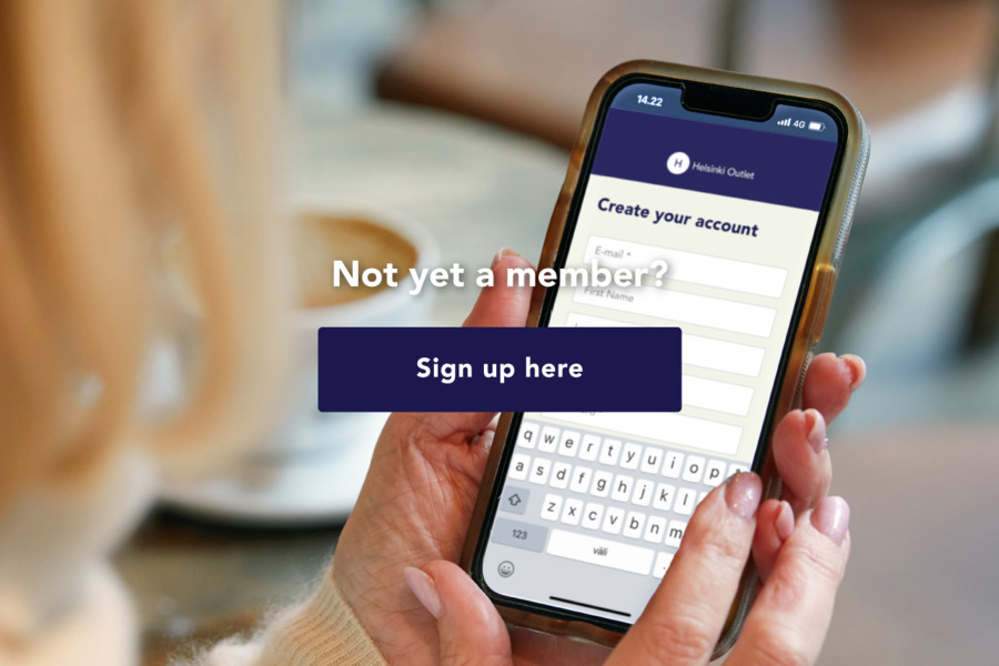 Close-up of hands holding a smartphone. The screen shows the Helsinki Outlet app registration page with the heading "Create your account". Text over the image reads: "Not yet a member? Sign up here".