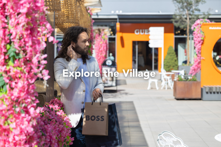 A man wearing a light blazer and holding a BOSS bag is enjoying a summery shopping village