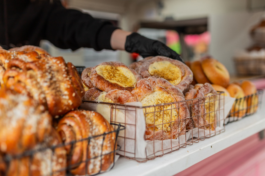 Pullabiili Close-up of bread baskets filled with fresh pastries and buns. A gloved hand is handing out a pastry to a customer.