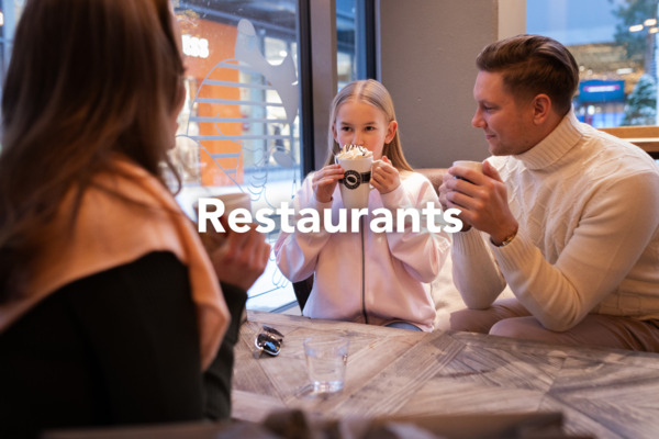 A girl is drinking hot chocolate with whipped cream, and her mom and dad are sitting with her around the table