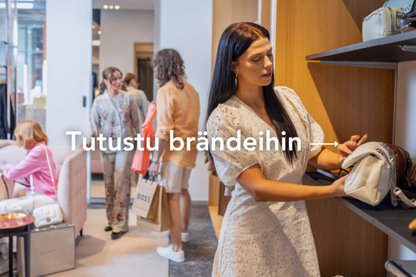 Nainen ihastelee ostoskylän myymälässä valkoista käsilaukkua taustalla muita ihmisiä