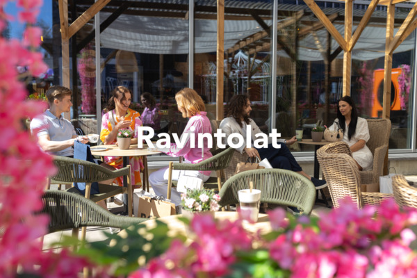 Terassiravintola värikkäiden kukkien keskellä, pöytiä ja tuoleja asiakkaita varten. Kuvassa lukee “Ravintolat”.