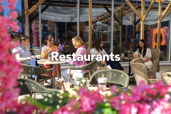 An outdoor restaurant surrounded by colorful flowers, with tables and chairs set up for customers. The image is labeled “Restaurants”.