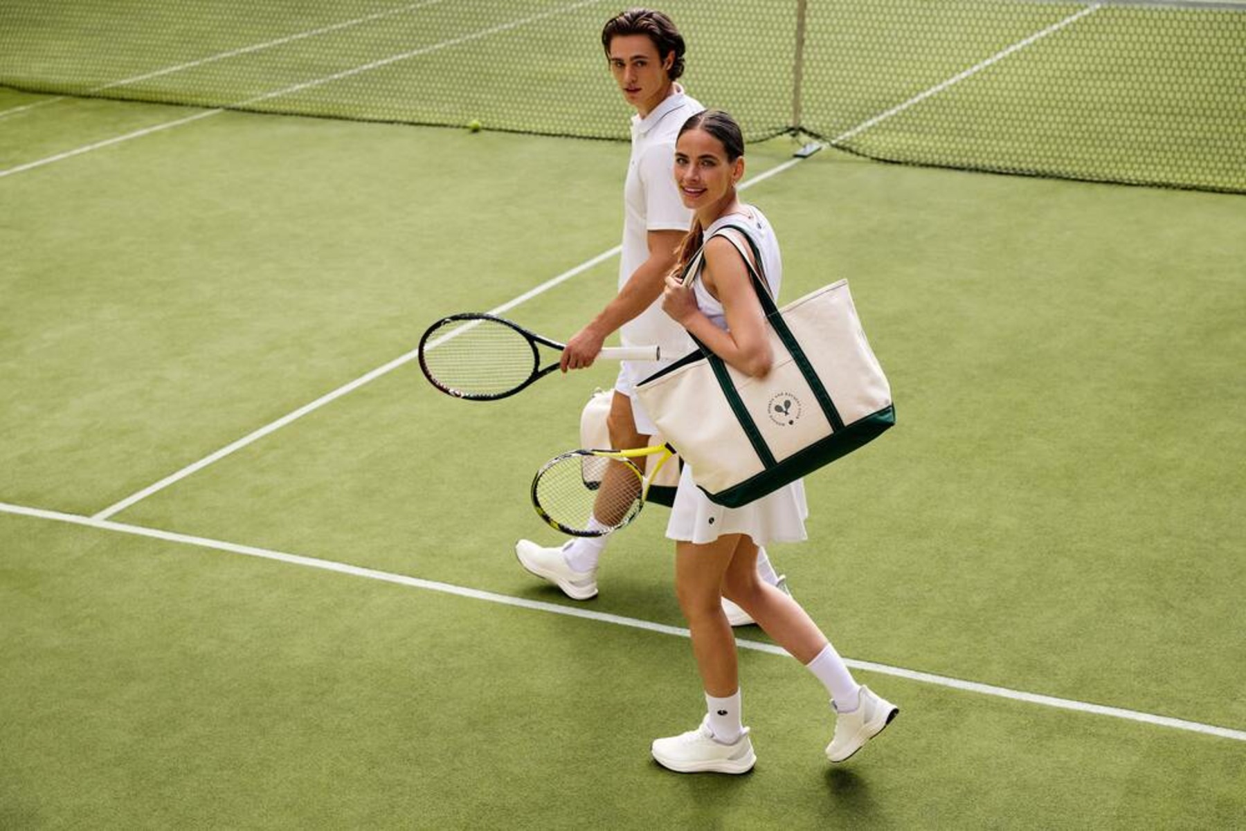 Mies ja nainen valkoisissa tennisvaatteissa kävelemässä pelikentällä