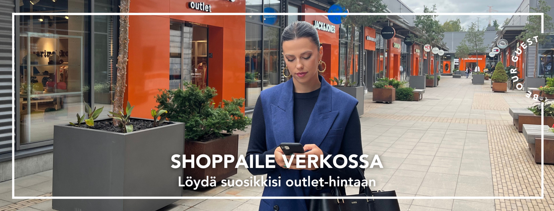 Nainen tyylikkäissä vaatteissa selaa puhelinta ostoskylän kadulla