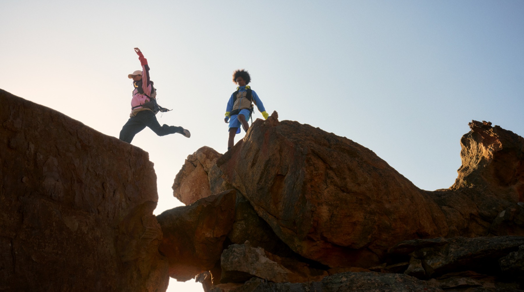 Two people high up in the mountains. One of them jumping over a gap.